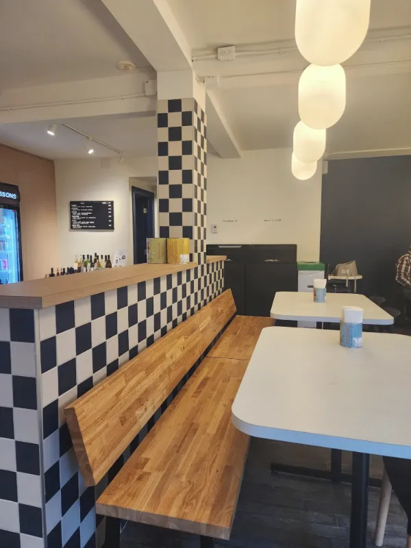 Longue banquette en bois adossée au muret en damier, sous des luminaires en globe