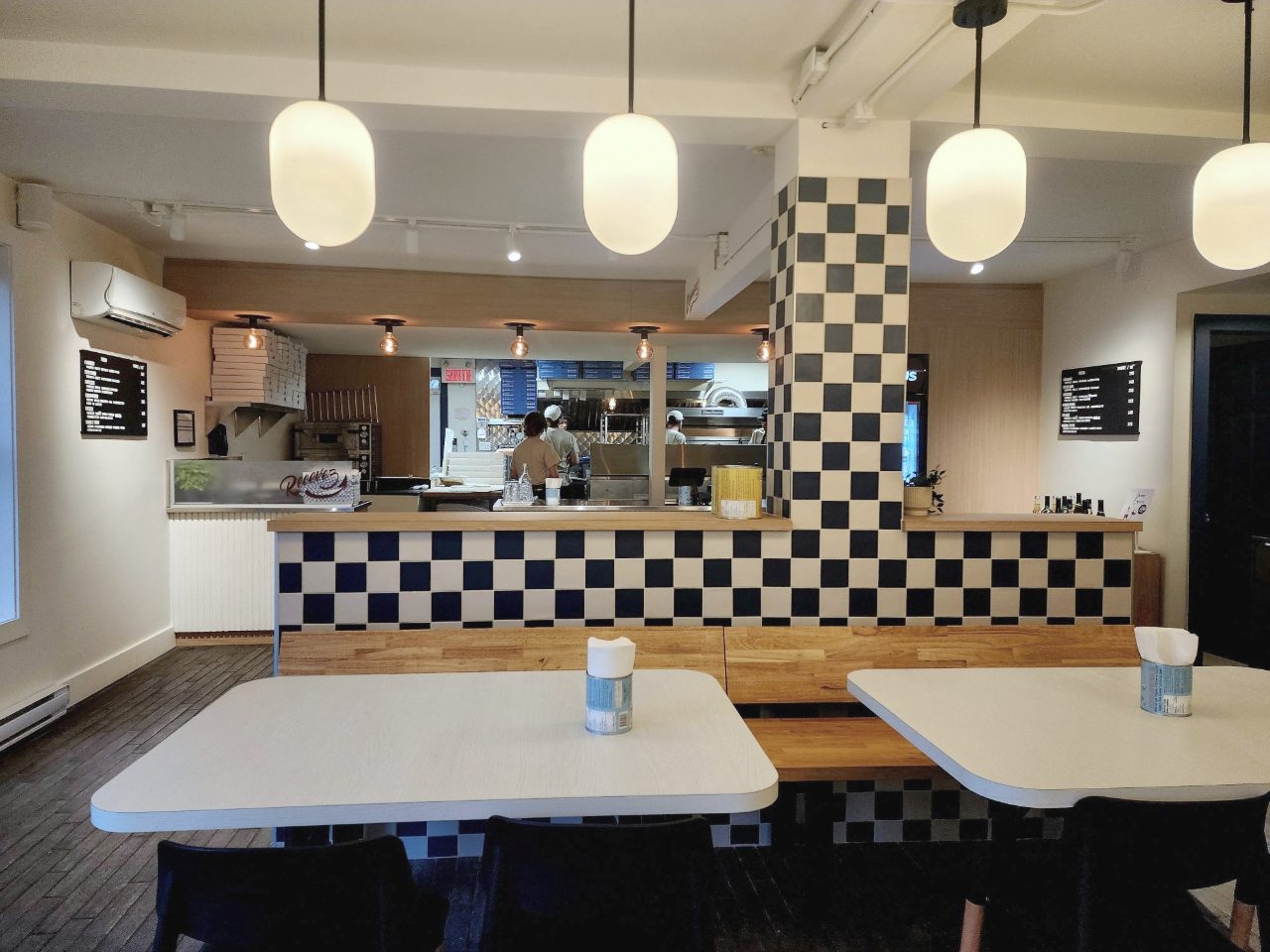 Salle de Paul Pizza : comptoir en carreaux marine et crème, globes lumineux et cuisine ouverte au fond