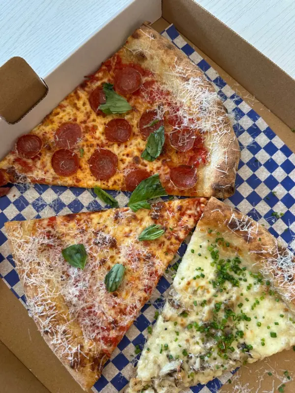 Pointes de pizza pepperoni, fromage et champignon dans une boîte doublée de papier à damier bleu