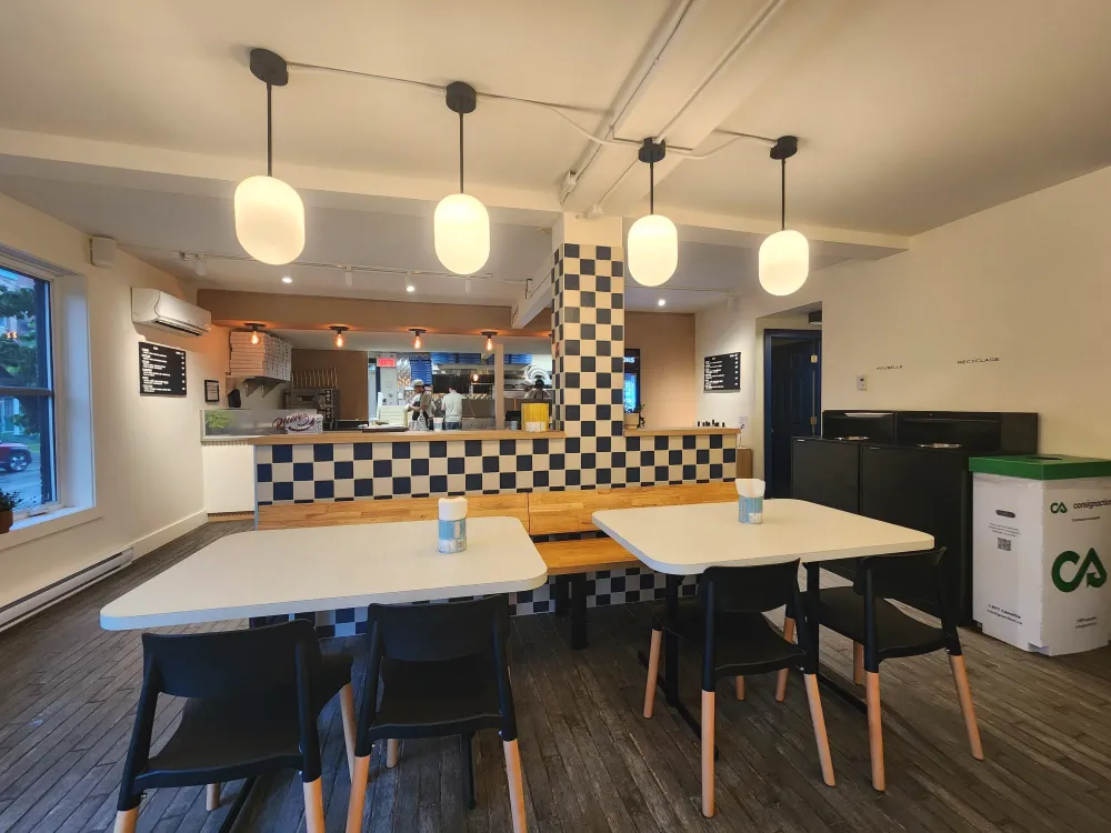 Vue d'ensemble de la salle : tables blanches, chaises noires et comptoir en damier